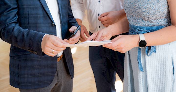 Tśi wósoby w businessowej drastwje pśepódaju sebje łopjeno papjery, jadna wósoba źaržy šmóratko.