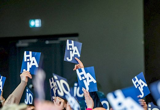 Mehrere Personen heben blaue Abstimmungskarten mit den weißen Buchstaben 