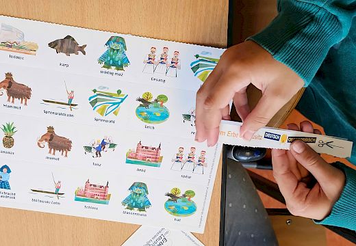 Góle źaržy šlapku papjery z tekstom nad łopjenom z wobrazami, kótarež su ze serbskimi a nimskimi mjenjami pópisane