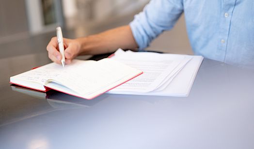 Wósoba w módrej zgło pišo z běłym pisakom do wótwórjonego zapisnika na bliźe z dalšnymi papjerami