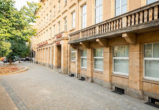 Serbski dom z pěskowcowym wobłoženjom a wulkimi woknami na plestrowanym chódniku ze štomami a nadróžnymi lampami