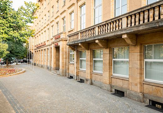 Haus der Sorben mit Sandsteinverkleidung und großen Fenstern an einem gepflasterten Gehweg mit Bäumen und Straßenlaternen