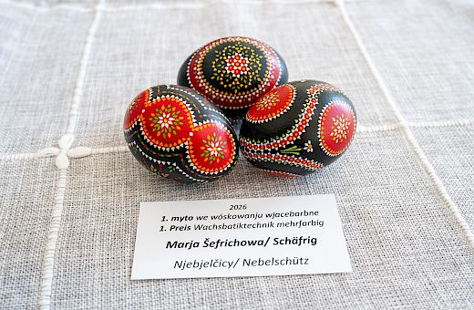 Tśi wěcejbarwne, z mandalowymi mustrami wupyšnjone wóskowe jaja na šerem suknje z płaśiznowej toflicku Betiny Borchering z Ramina; technika wóskowanja wjelebarwne