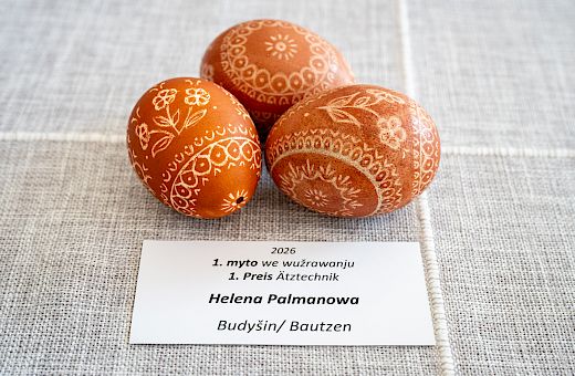Tśi wěcejbarwne, z mandalowymi mustrami wupyšnjone wóskowe jaja na šerem suknje z płaśiznowej toflicku Betiny Borchering z Ramina; technika wóskowanja wjelebarwne