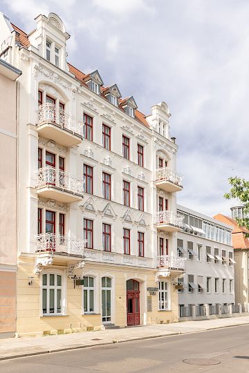 Serbski dom w Chóśebuzu z wupyšnjonymi balkonami, cerwjenymi woknowymi ramikami a cerwjenymi zachodnymi źurjami pśi měrnej droze.