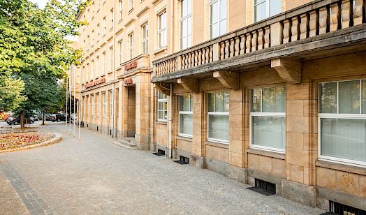 Haus der Sorben mit Sandsteinverkleidung und großen Fenstern an einem gepflasterten Gehweg mit Bäumen und Straßenlaternen