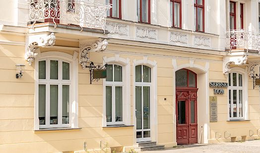 Wendisches Haus in Cottbus mit gelb gestrichener Putzfassade, weißen Fenstern, roten Türen und zwei schmiedeeisernen Balkonen